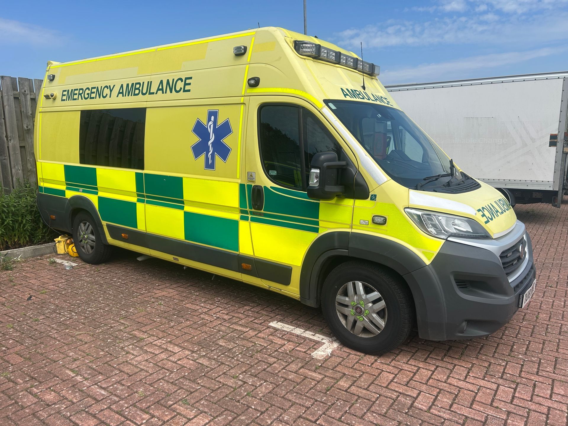 A bright yellow and green ambulance with a blue Star of Life symbol parked on a paved lot in daylight.