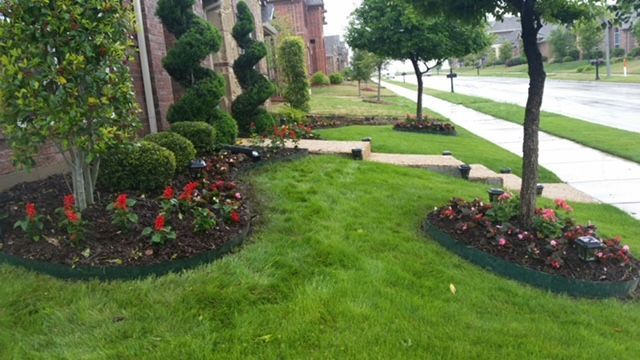 Lush green lawn with flower beds beside a sidewalk and street on a rainy residential corner