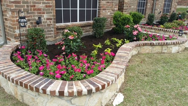 Curved brick flower bed with pink and white blooms along a house exterior
