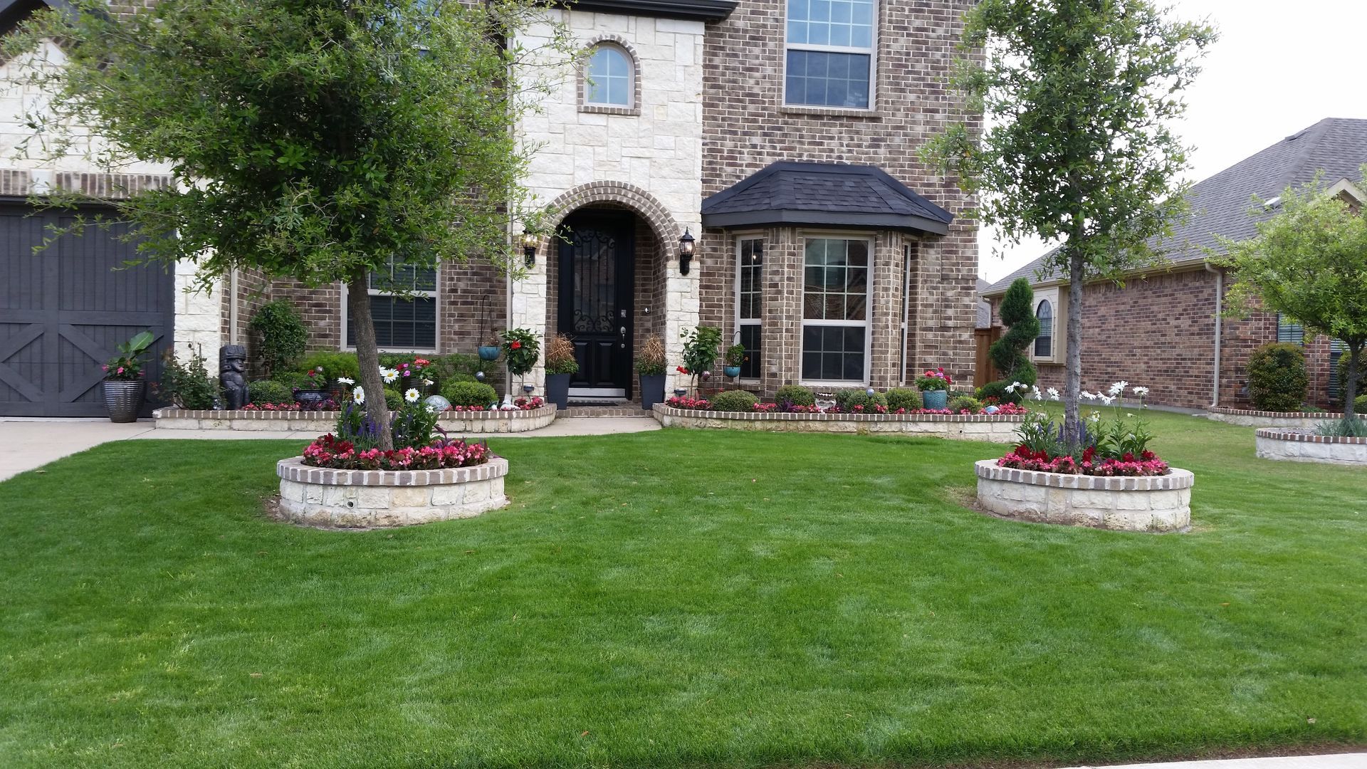 Stone house with arched entry, manicured lawn, and flower planters in front yard