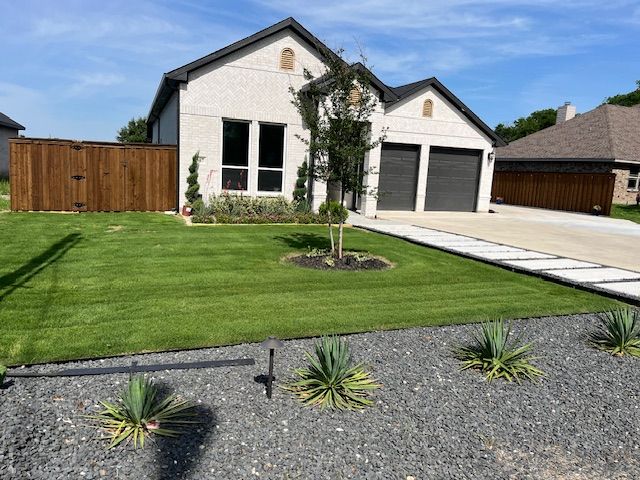 Modern white house with two garages, manicured lawn, and gravel landscaping under a blue sky