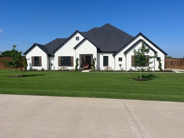 Single-story white suburban house with dark roof and large green lawn under a clear sky