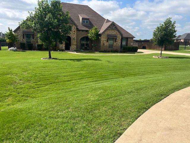 Large brick house with a well-manicured green lawn and curved driveway under a clear sky