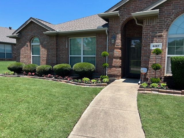 Brick suburban house with manicured lawn, arched windows, and a curved concrete walkway