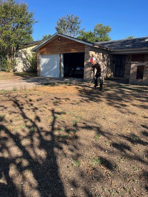 Person standing outside an open garage beside a brick house under trees.