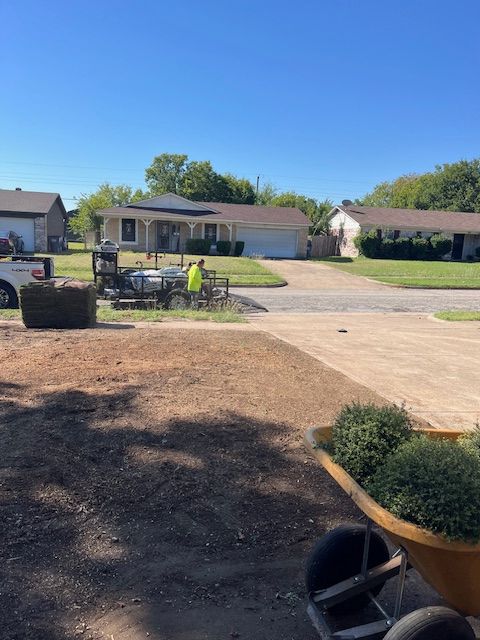 Suburban front yard with workers and equipment beside a driveway under a clear blue sky
