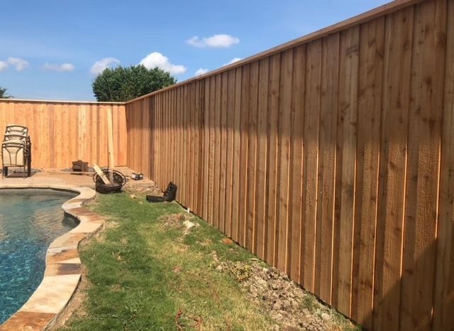 Backyard pool beside a long wooden privacy fence and grass strip under a blue sky