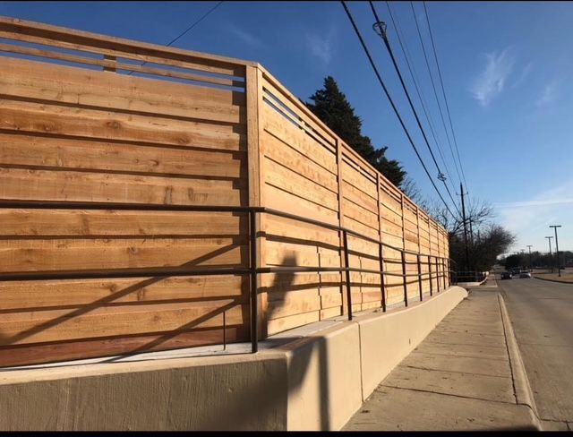 Wooden sound barrier wall along a sidewalk beside a road on a sunny day