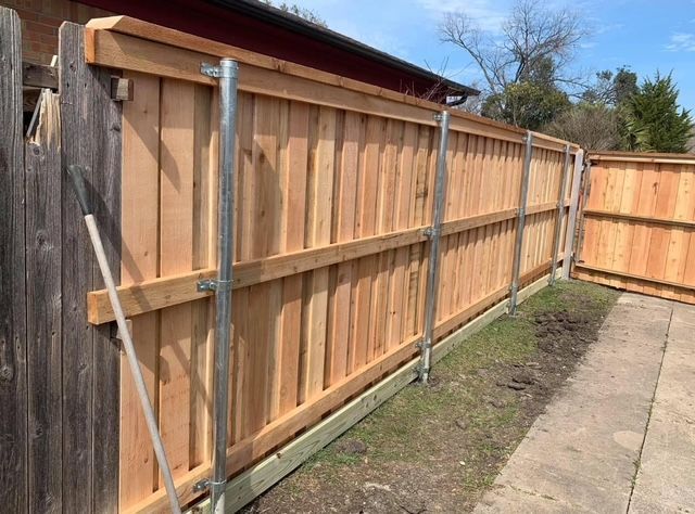 Wooden privacy fence along a sidewalk beside a house and narrow dirt strip