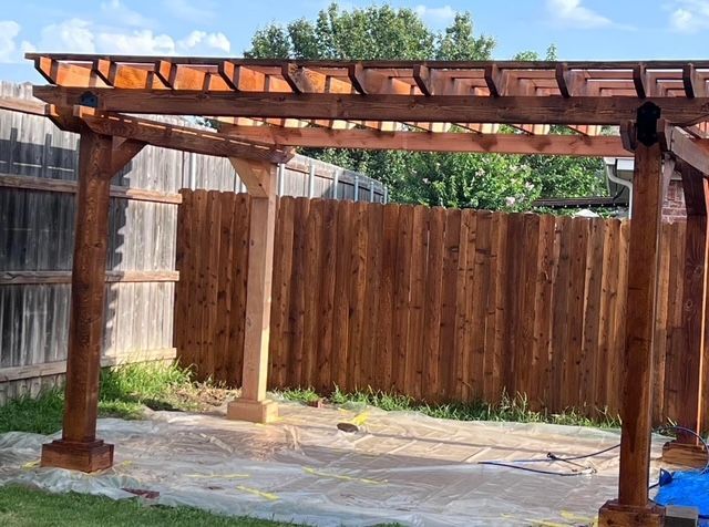 Wooden backyard pergola with posts and lattice roof over a paved patio against a privacy fence