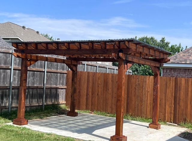 Wooden pergola with four posts in a backyard patio beside a fence