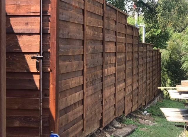 Wooden privacy fence along a grassy path beside trees in a sunny yard