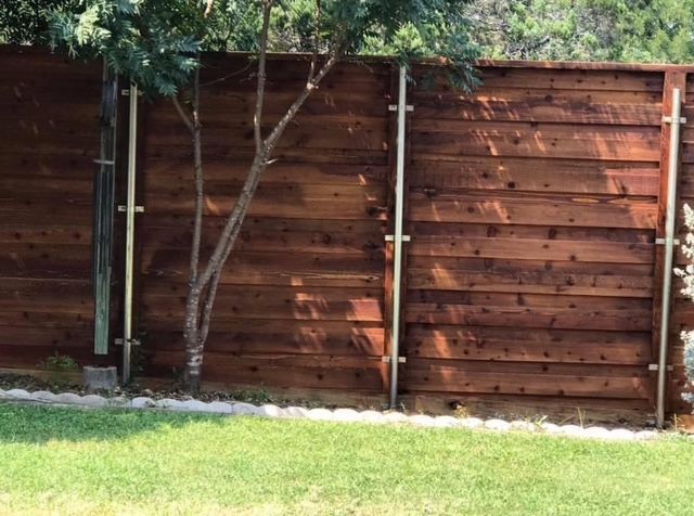 Wooden backyard fence with a thin tree in front and green grass below
