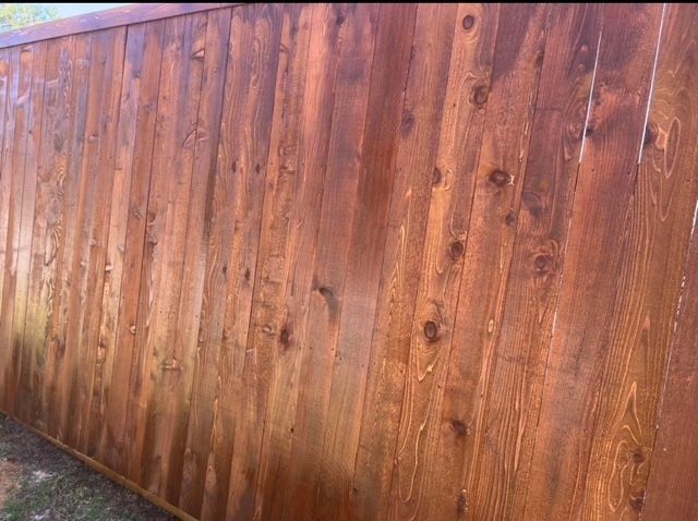 Wooden fence with vertical brown planks, stained and weathered, viewed at an angle.