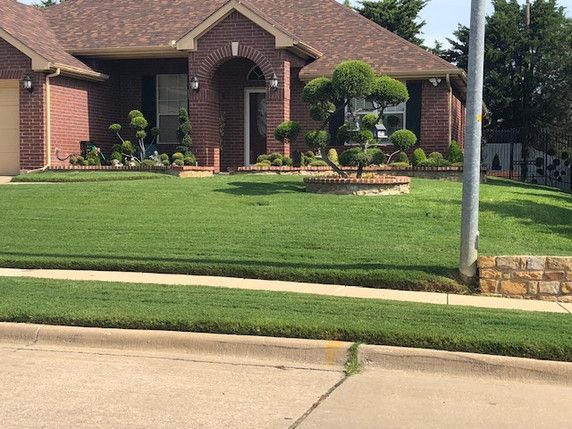 Brick house with manicured lawn, shrubs, and a front walkway by the street.