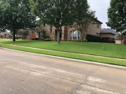Suburban brick house with a large green lawn beside a quiet street