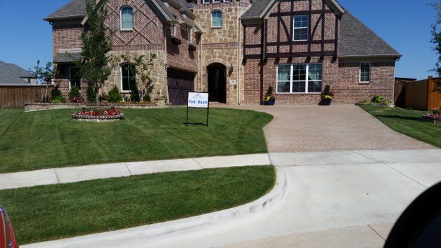 Large brick suburban house with a manicured lawn and a driveway in front.