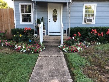 Front walkway to a white house with a flower-lined porch and front door.