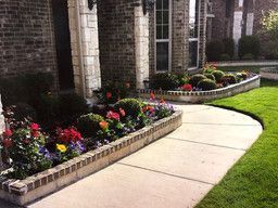 Curved sidewalk beside a stone building with colorful flower beds and manicured lawn