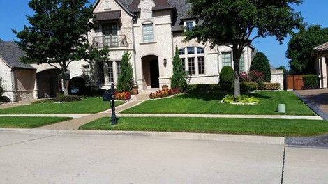 Suburban house with a stone facade, manicured lawn, and a driveway on a sunny day