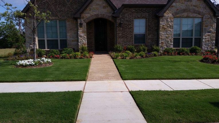 Brick house front entry with walkway, manicured lawn, and flower beds