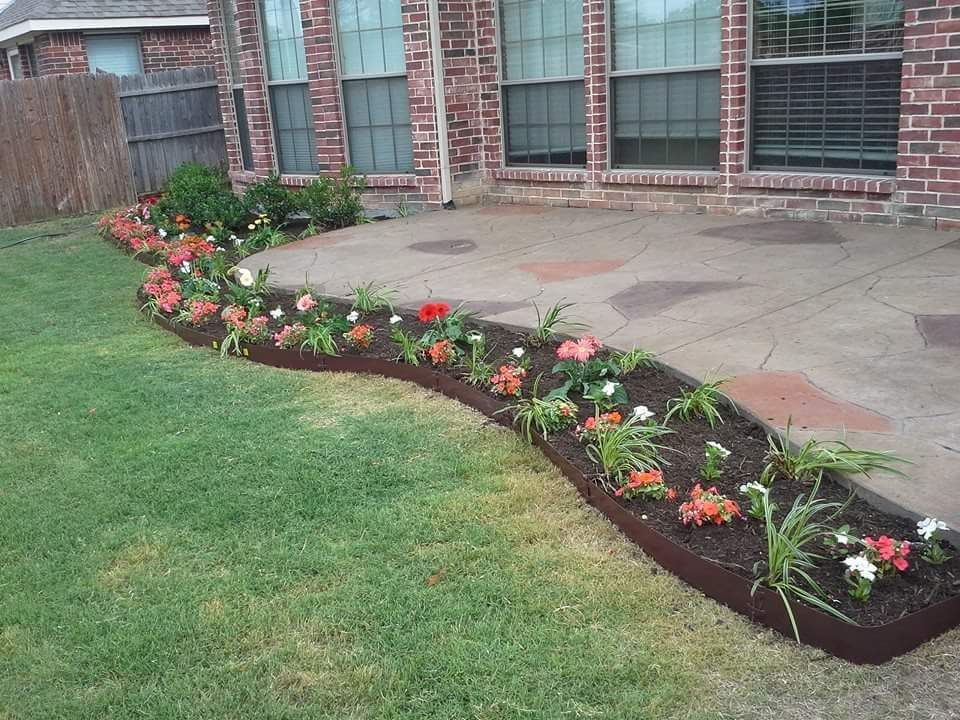 Curved flower bed with red and white flowers along a brick house patio and green lawn