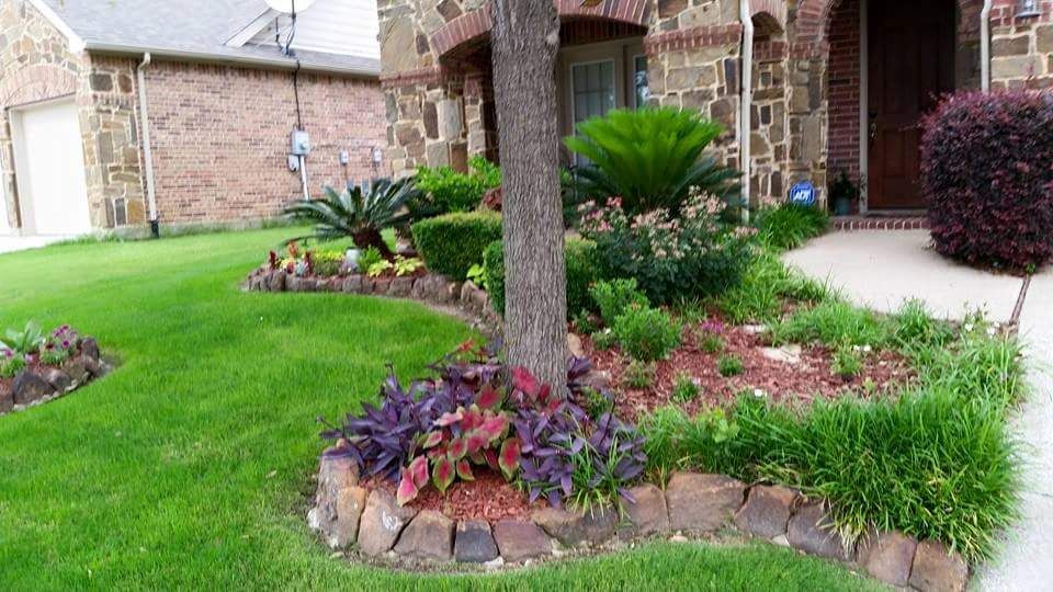 Landscaped front yard with trimmed lawn, colorful flower beds, and a tree by a brick house