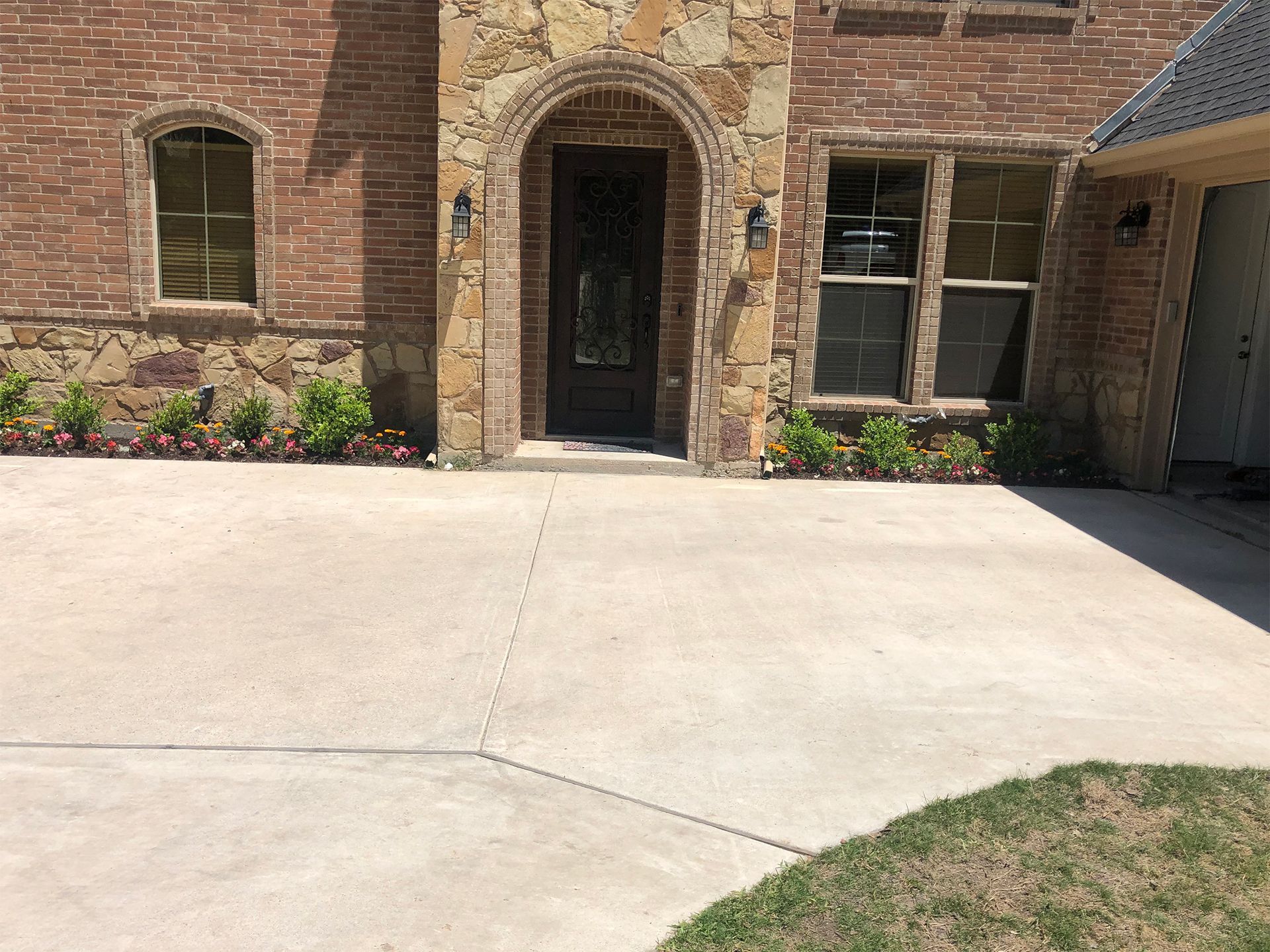 Brick house entrance with arched doorway, windows, and a concrete driveway in front