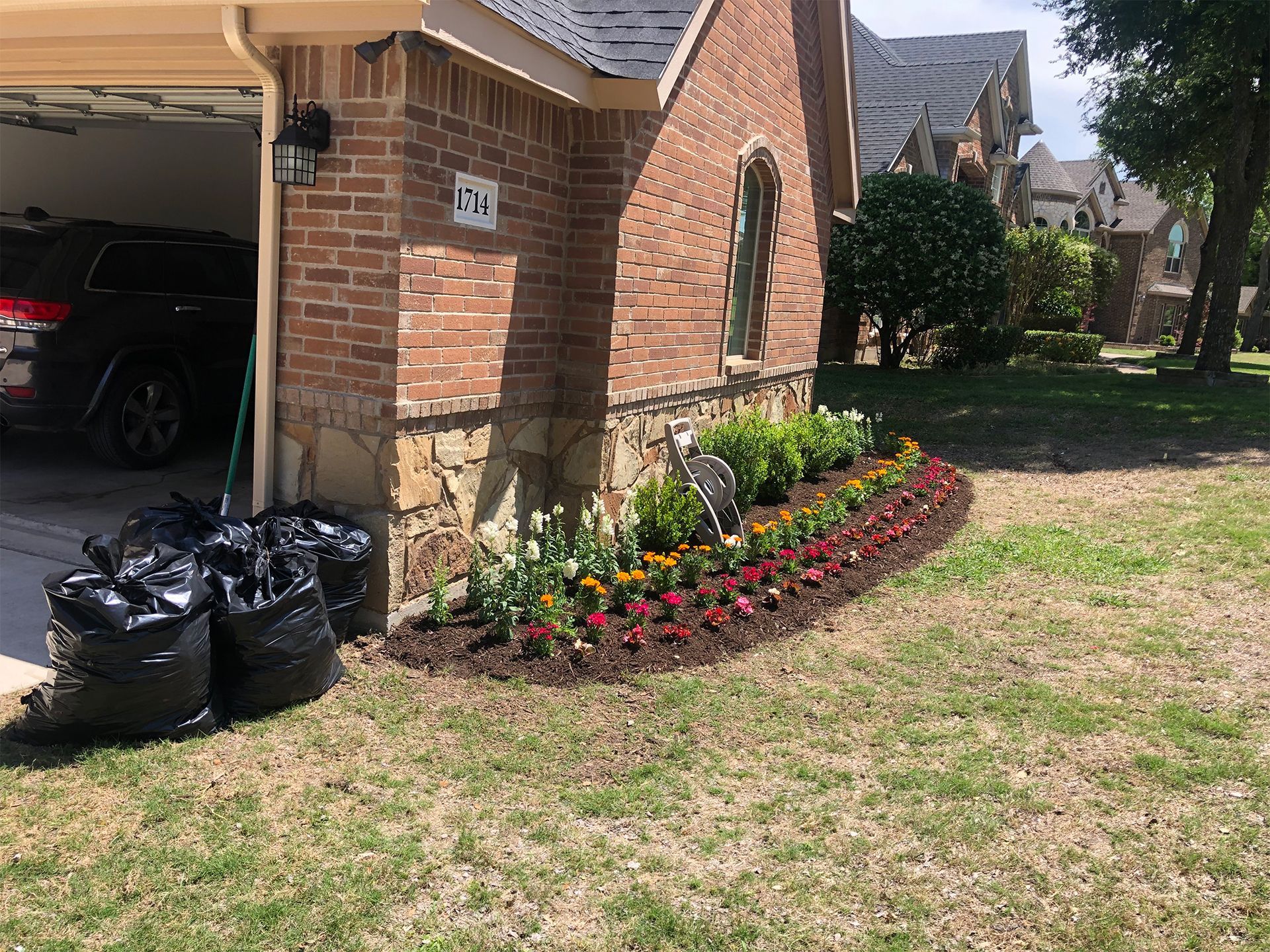 Brick house corner with colorful flower bed beside garage and lawn