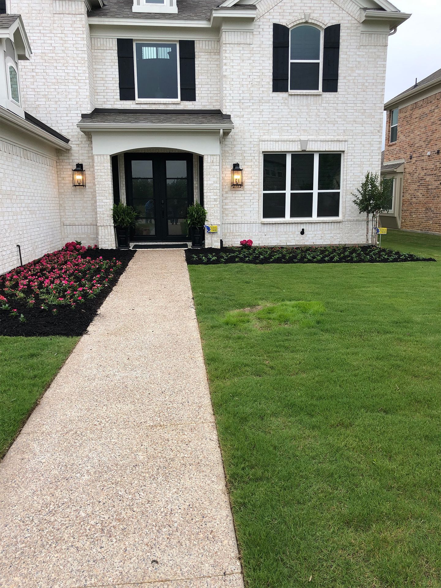 White brick house with black shutters, front walkway, and landscaped lawn and flower beds