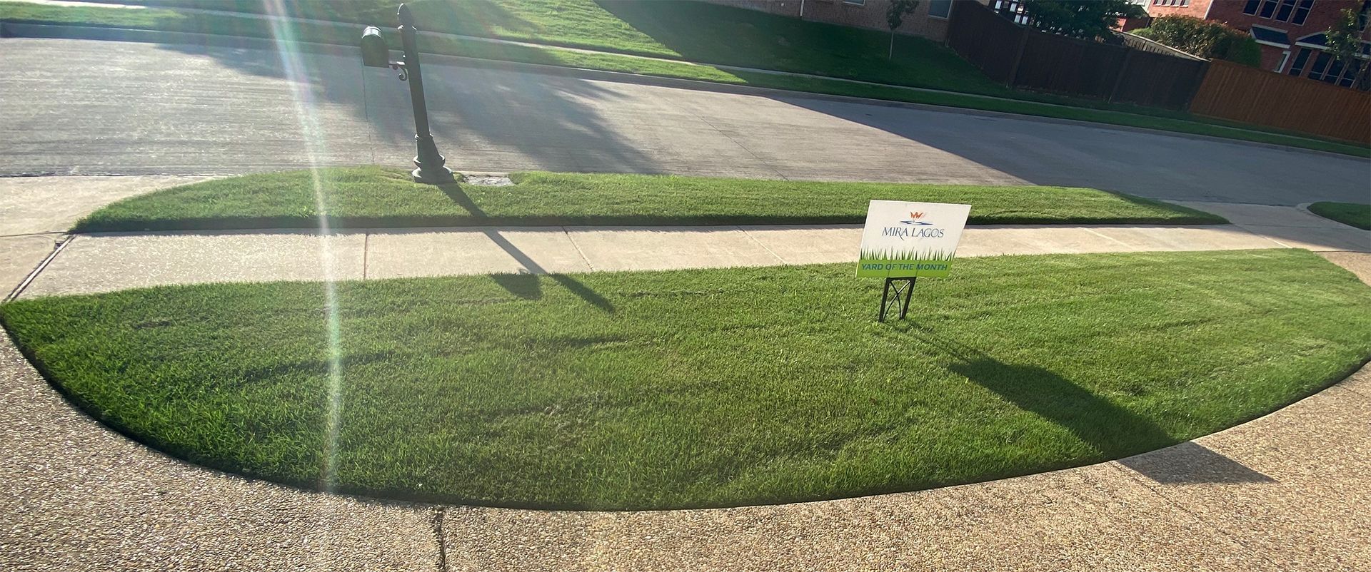 Front yard with a freshly mowed circular green lawn and a small sign near the sidewalk