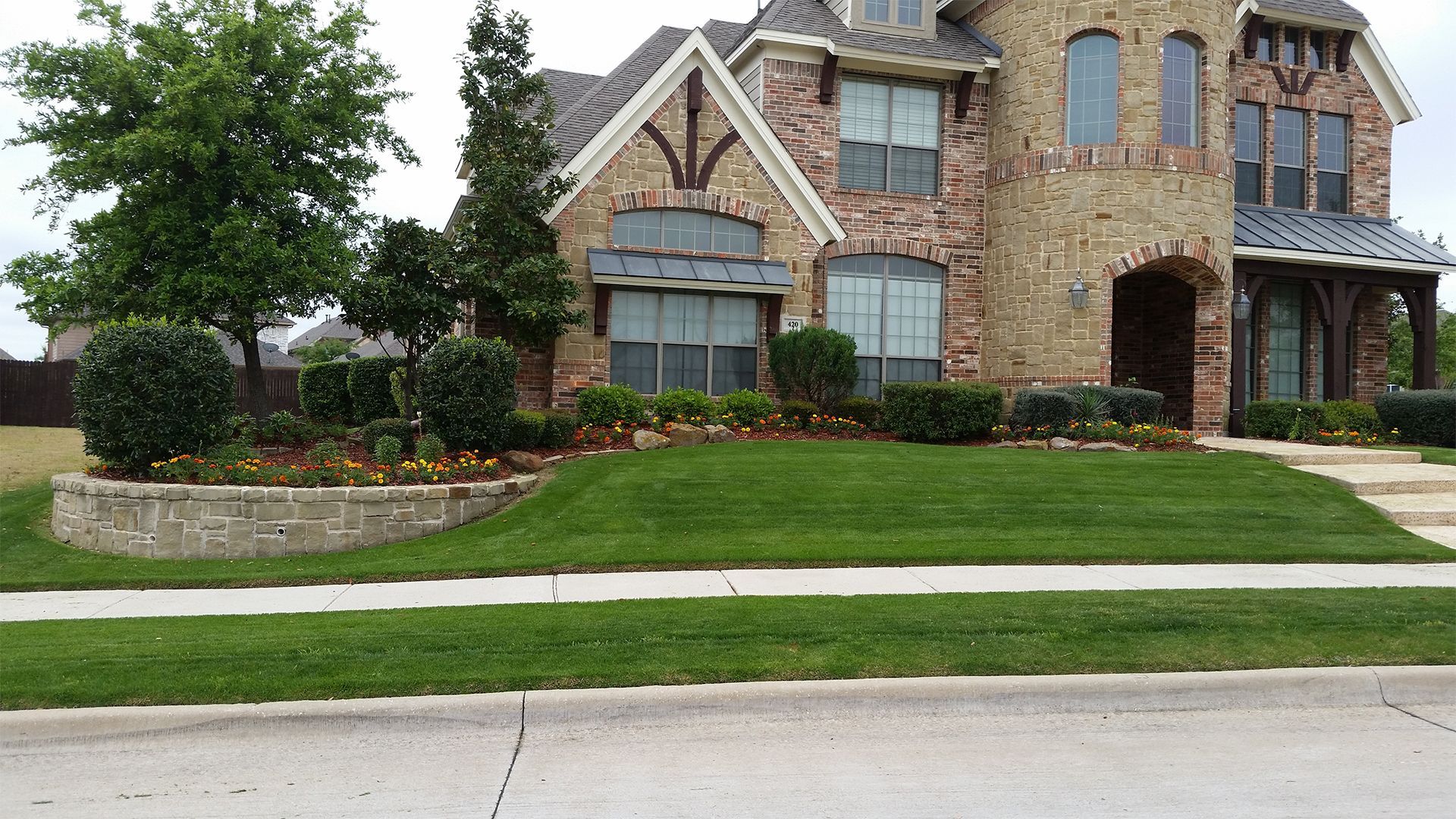 Large stone-and-brick suburban house with a manicured lawn and landscaped front yard