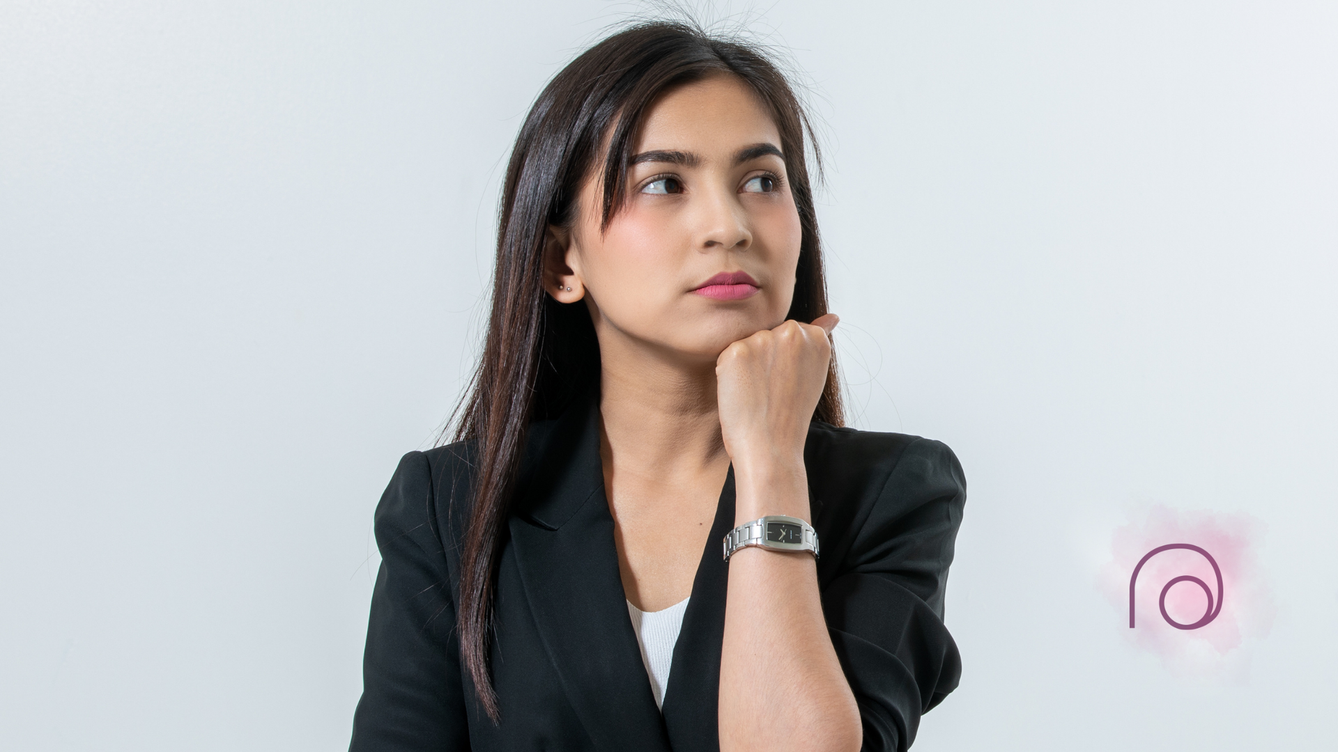 Woman in blazer, hand on chin, looking thoughtful, neutral background.