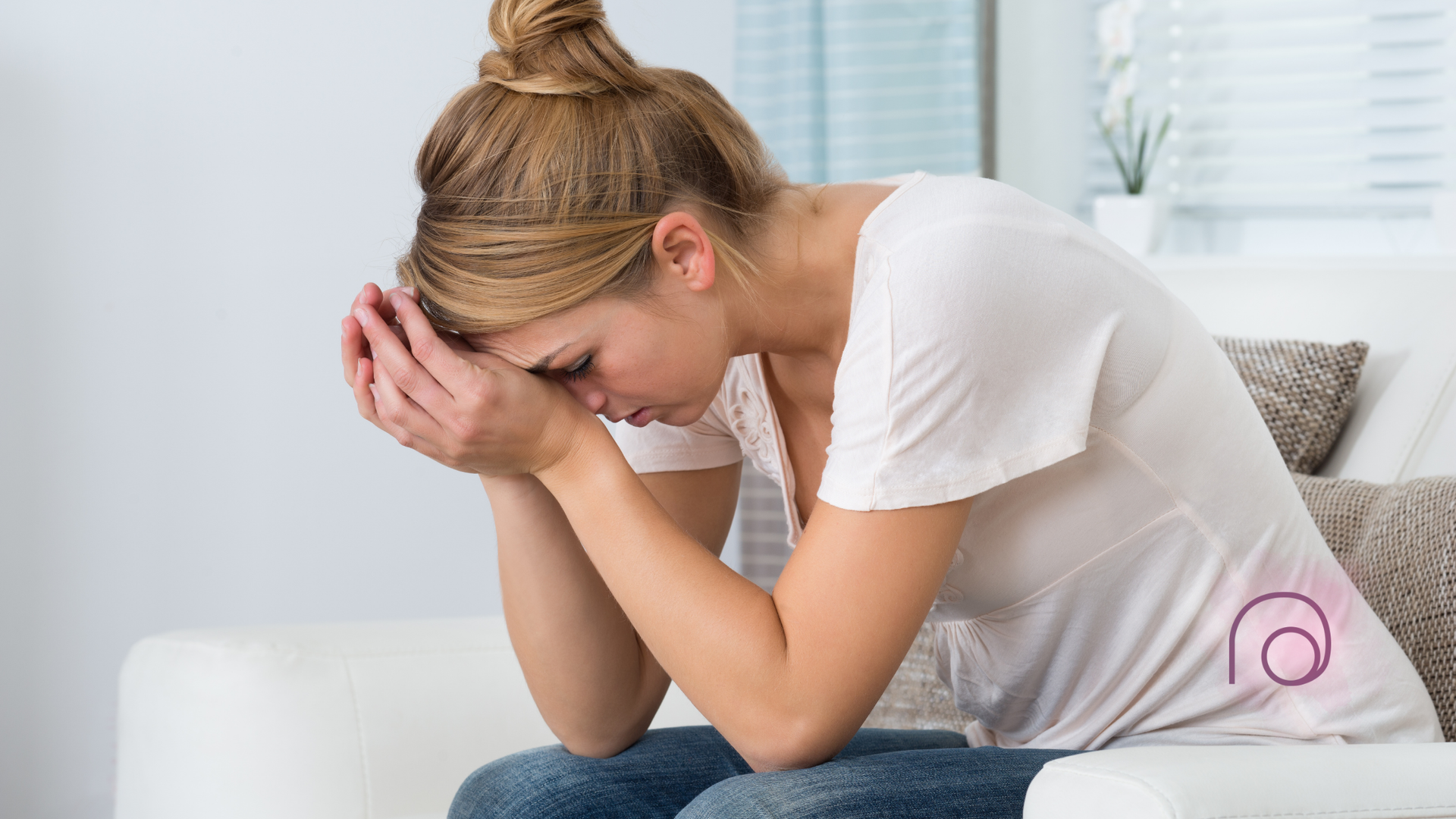A woman is sitting on a couch with her head in her hands.