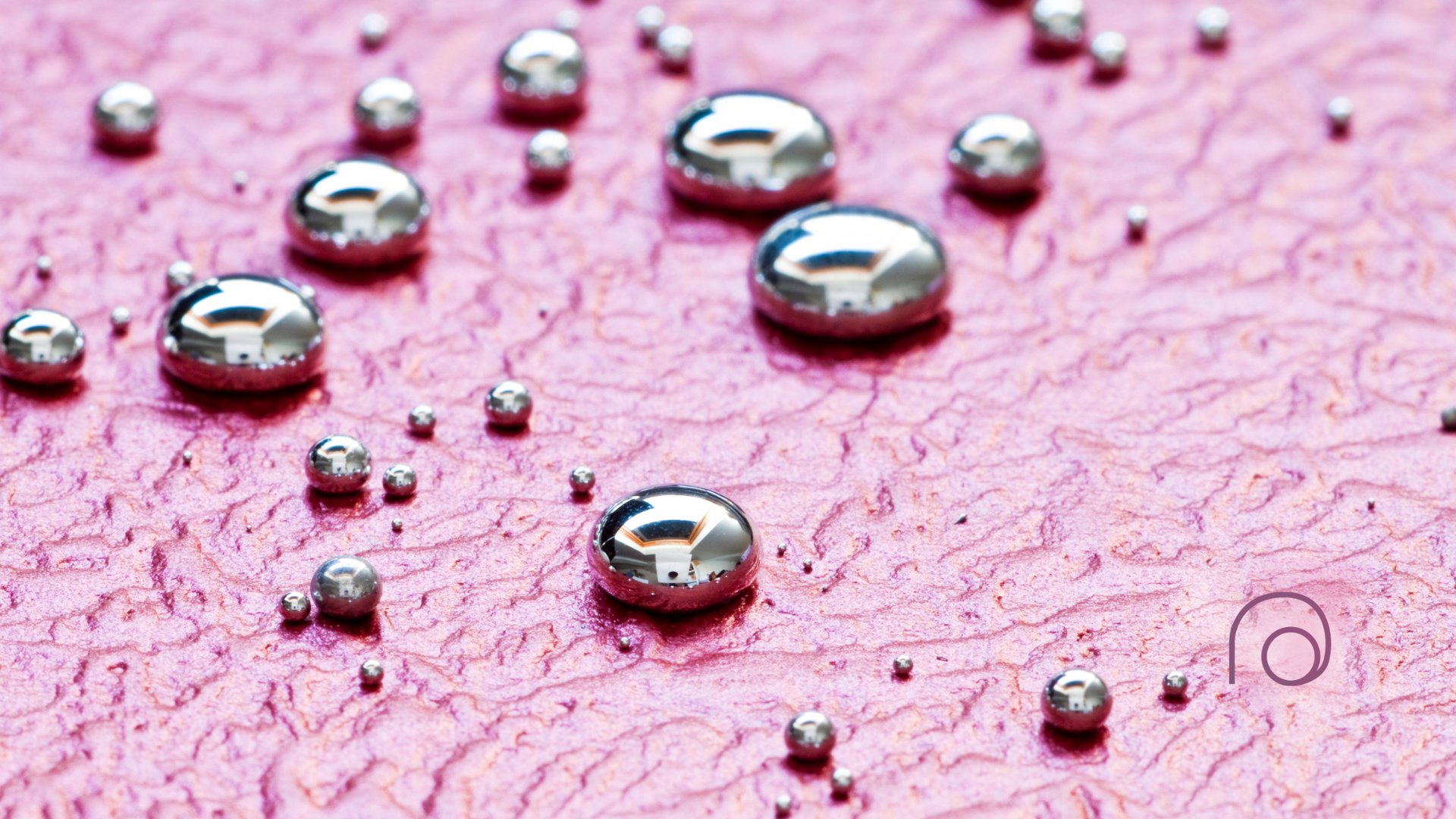 A close up of water drops on a pink surface.