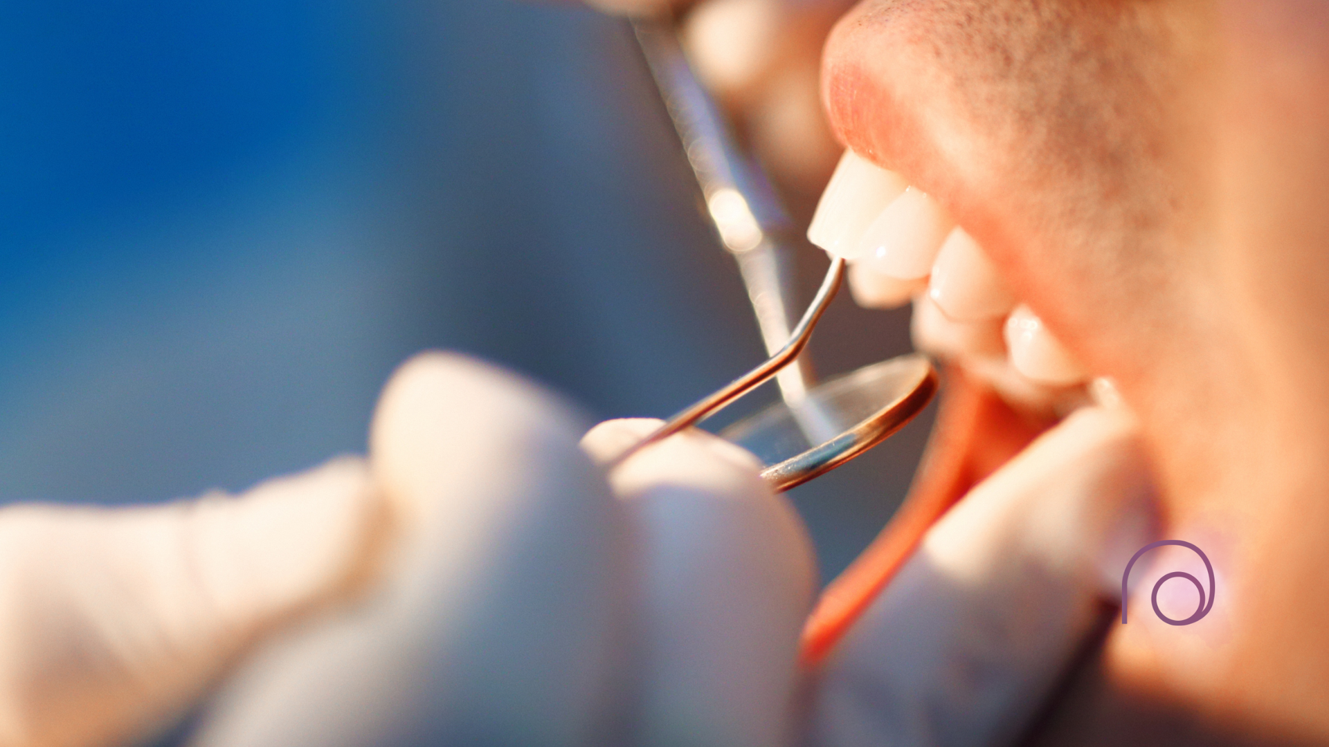 A dental professional’s gloved hands use a metal explorer and mirror to examine a patient's teeth.