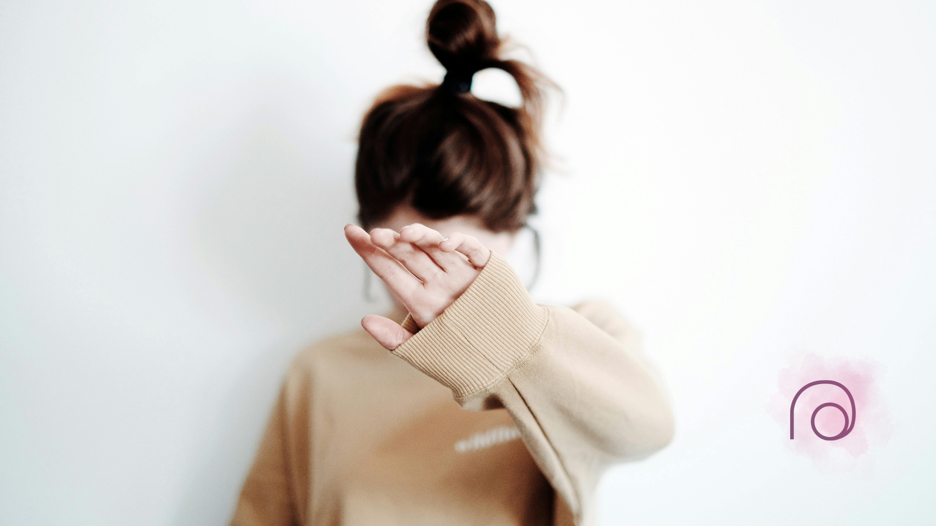 A woman in a tan sweater is covering her face with her hand.