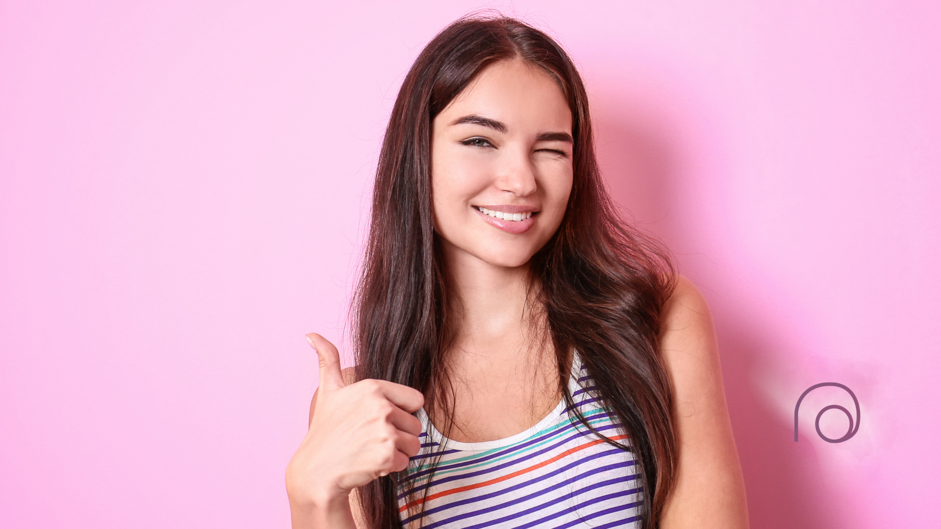 Woman winking and giving thumbs-up against a pink background, wearing striped tank top.