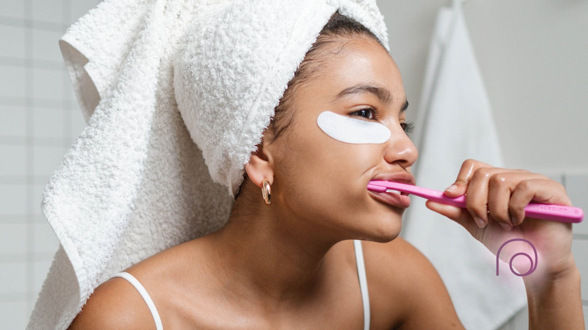 A woman with a towel wrapped around her head is brushing her teeth in the bathroom.