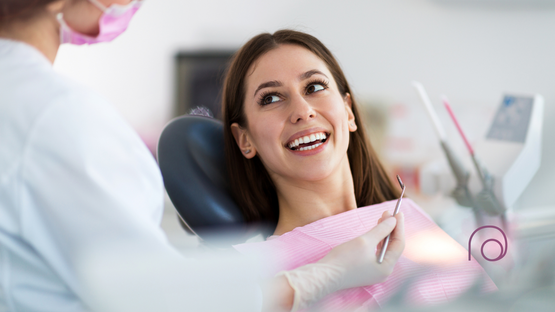 A person smiling while sitting in a dentist’s chair during an appointment, with a clinician visible in the foreground.