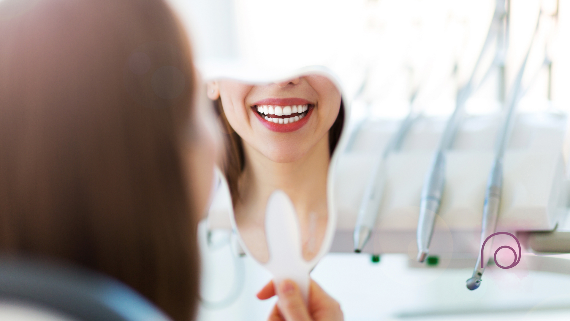 A patient holding a handheld mirror to view their bright, healthy smile in a dental office setting.
