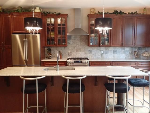 Modern kitchen with stainless steel fridge, wood cabinets, and white island with bar stools and hanging lights