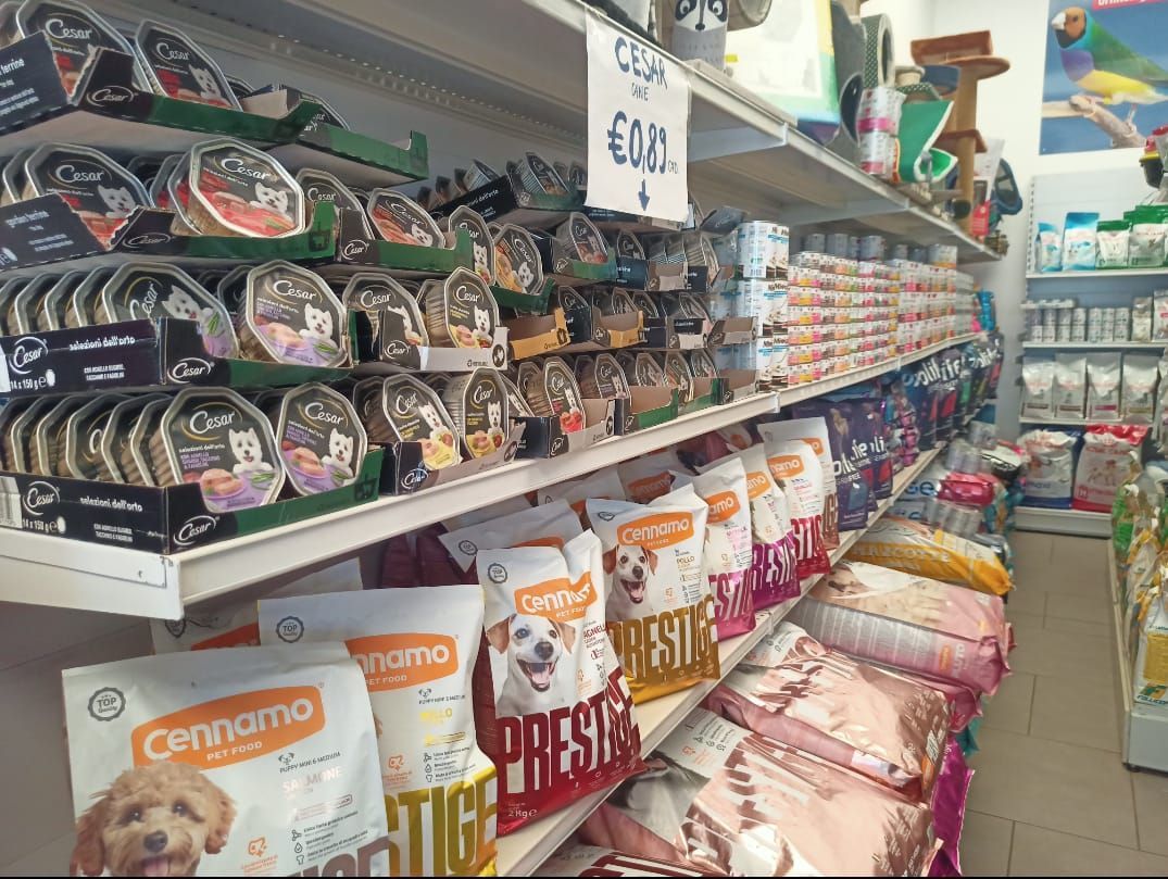 Corridoio di un negozio di animali con file di sacchetti di cibo per animali, scaffali di snack e un cartello con il prezzo.