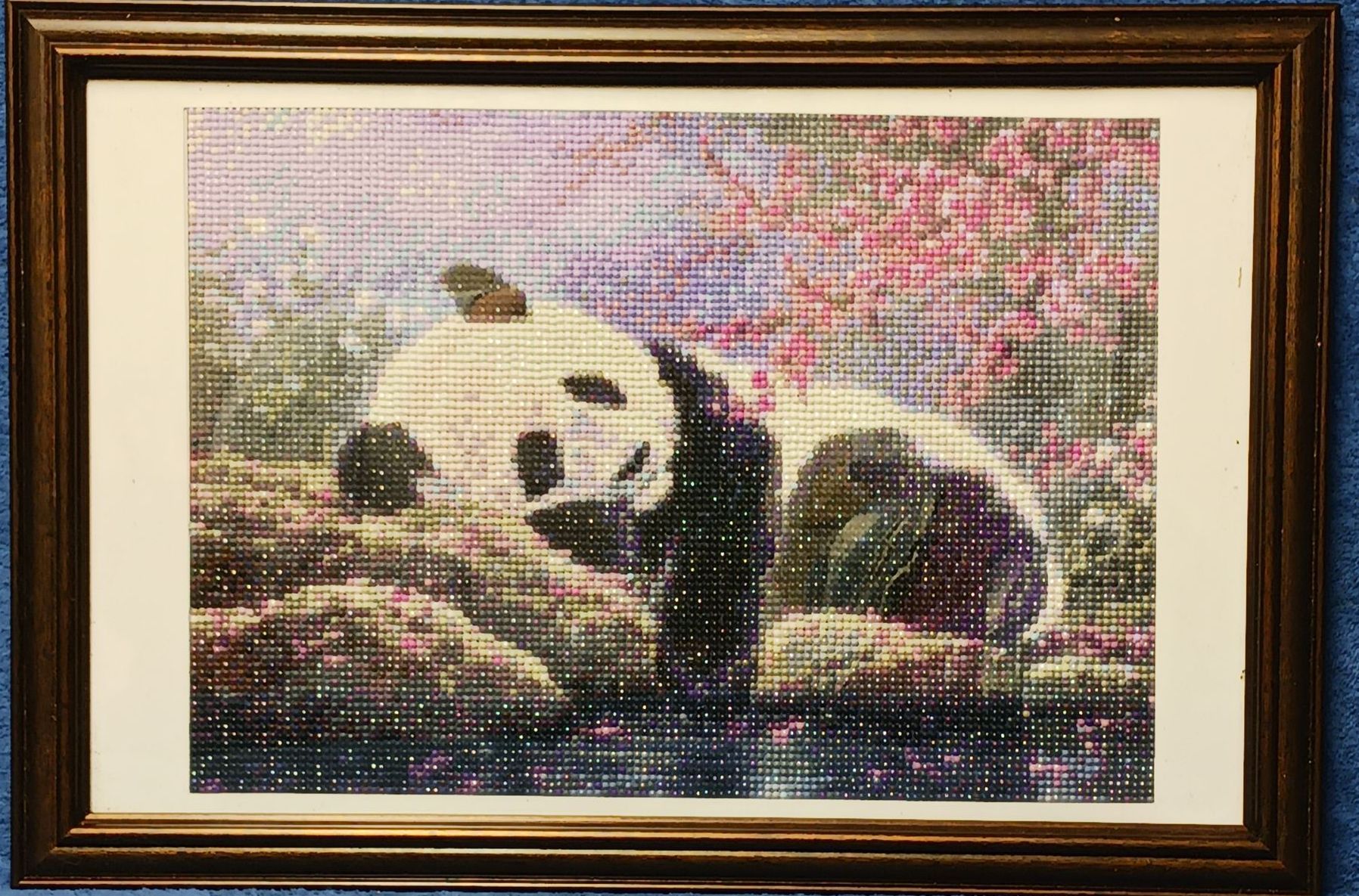 A framed diamond painting of a panda bear laying on a rock