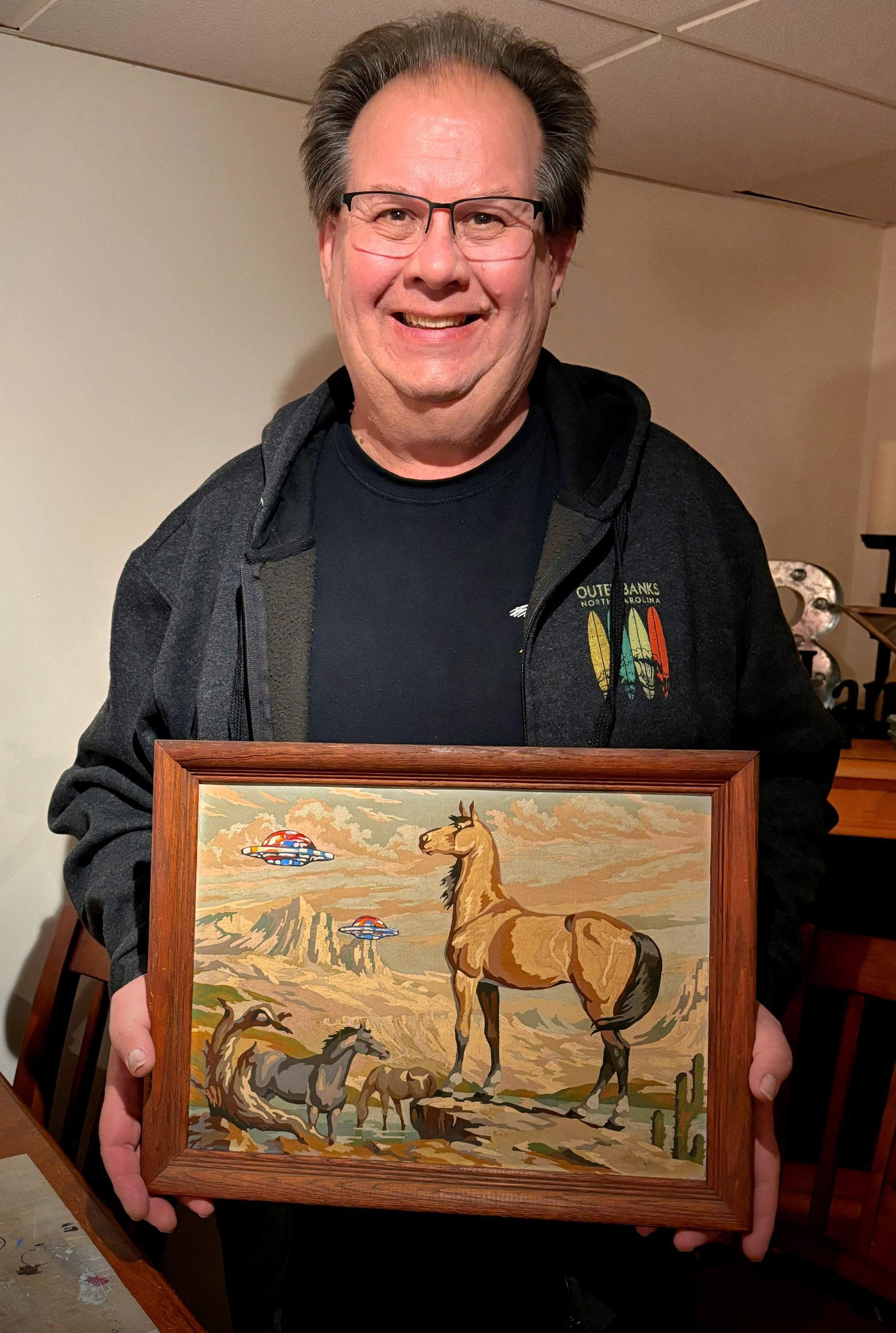 A man is holding a framed picture of horses