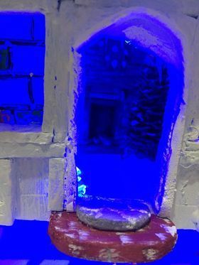 A gingerbread house model with a window with a blue light behind it.