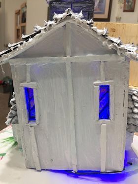 A cardboard gingerbread house with blue windows is sitting on a table.