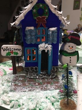 A blue gingerbread house with a welcome sign and a snowman.
