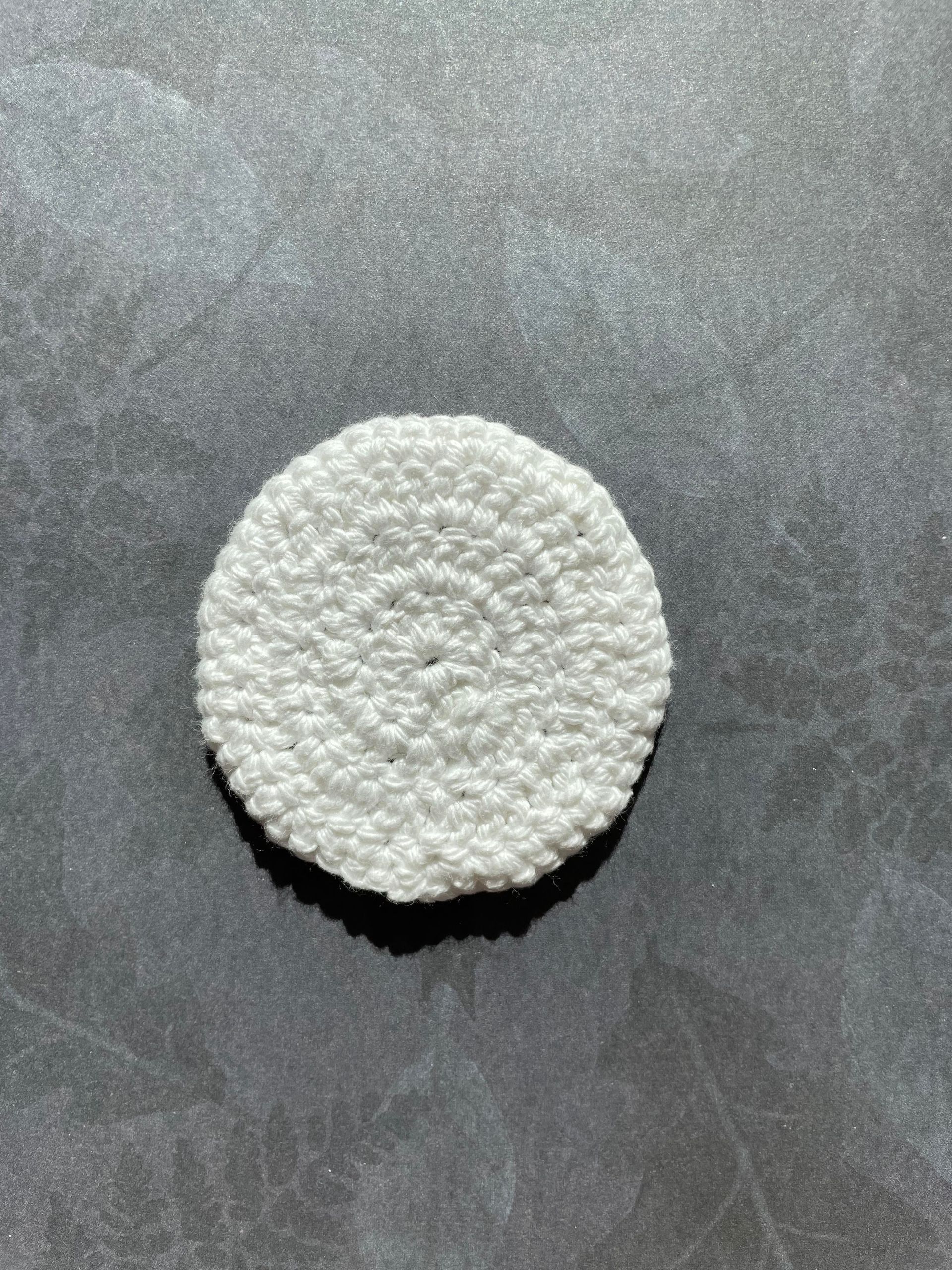 A white crocheted circle is sitting on a black surface.