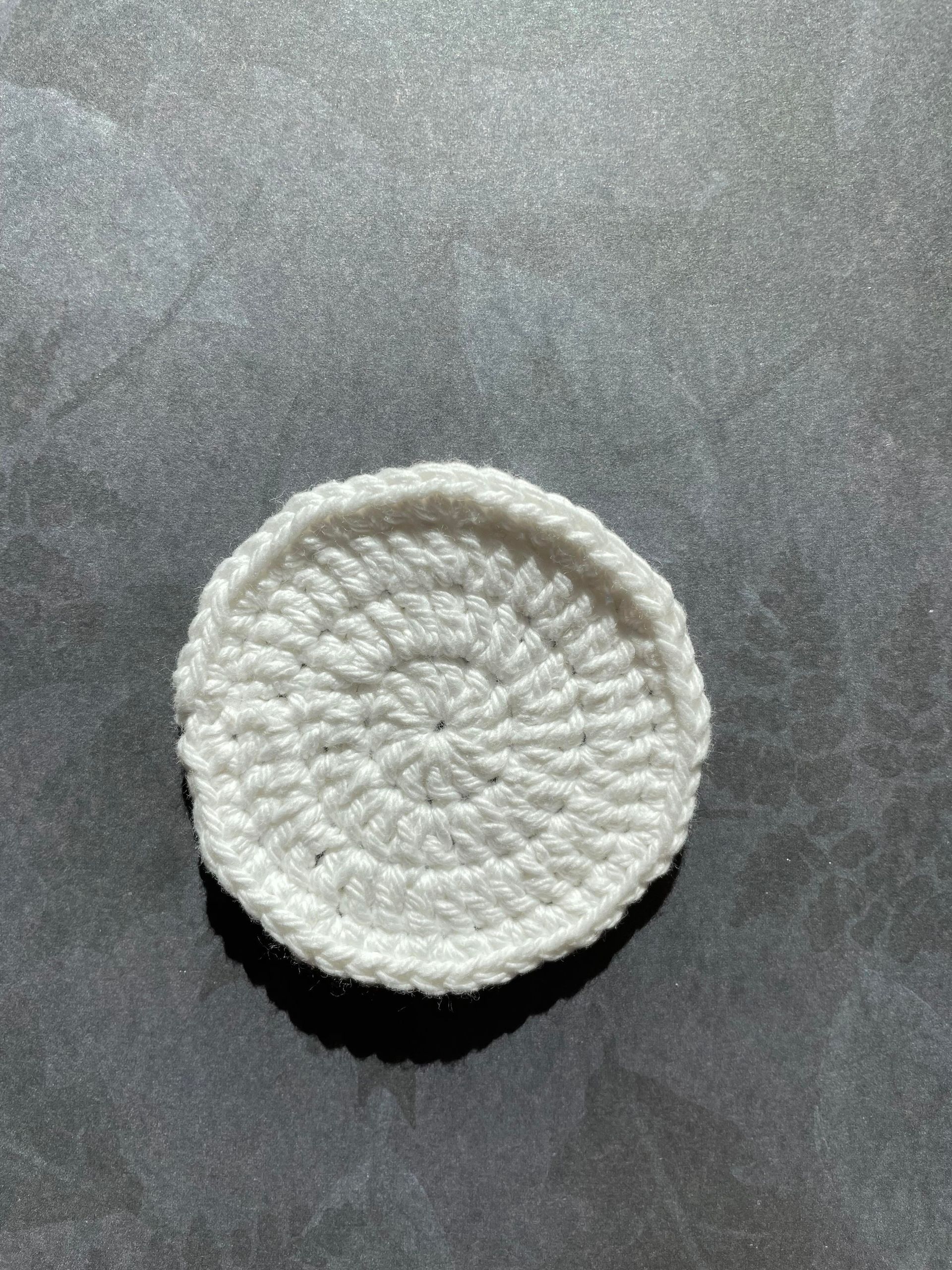 A white crocheted circle is sitting on a black surface.
